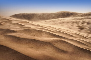 Lonely sand dunes in a strong wind under the sky against the background of arid desert
