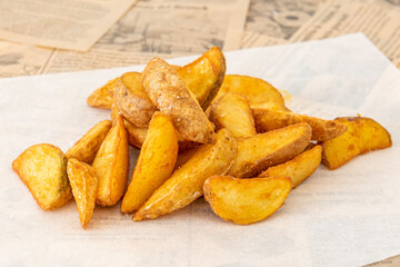 Portion of French fries cut into wedges with the skin and sea salt on white greaseproof paper