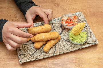 Chef's hands placing portion of fried Venezuelan tequeños on a log plate accompanied by a little guacamole with tortilla chips and pico de gallos