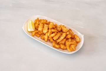 Copious portion of squid battered in panko and fried in virgin olive oil with a piece of lemon to garnish on a white marble table