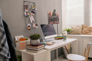 Interior of part of domestic room with desk, chair, computer, books, lamp and other stuff