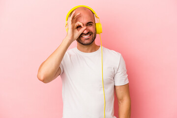 Young caucasian bald man listening to music isolated on pink background  excited keeping ok gesture on eye. © Asier