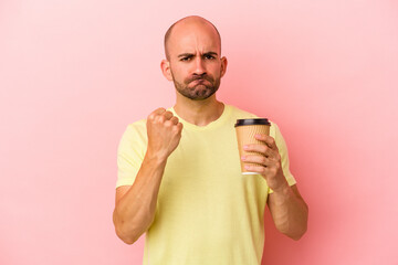 Young caucasian bald man holding a take away coffee isolated on pink background  showing fist to camera, aggressive facial expression.