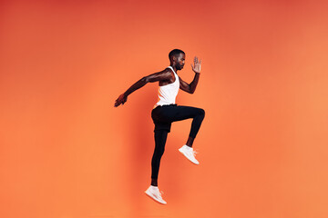 Fototapeta na wymiar Fit man jumping in studio. Male runnner warming up before workout against orange background