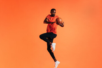 Fototapeta na wymiar Sportsman jumping in studio against an orange background with basket ball