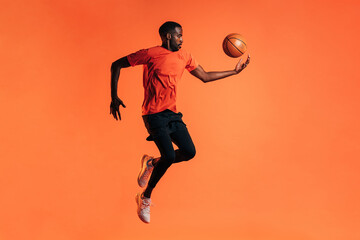 Fototapeta na wymiar Side view of young male jumping and throwing up a basket ball in studio