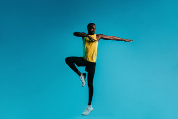 Fototapeta na wymiar Young man in sportswear jumping and stretching his arms over blue background