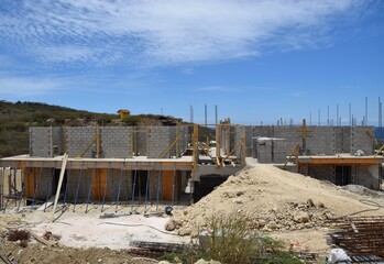 View of a building construction site with sand and block material, hillside and blue sky in the background