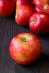 Fototapeta na wymiar Closeup a fresh ripe apple with blurry heap of red apples on black wooden background 