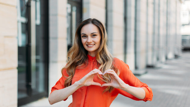 Caucasian girl smiles with hands makes a heart-shaped gesture as a symbol of love