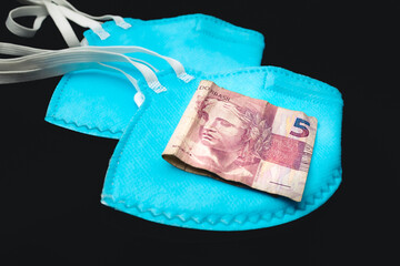 Cédula do Real brasileiro em meio a máscaras de proteção facial n95 de cor azul. Foto em...