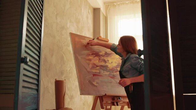 Female artist is working at picture using oil paints and palette-knife creating beautiful paints a picture. Painting technique and painters concept. Young girl artist painting with palette knife.