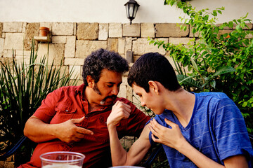 Teenager showing his biceps to his father at an outdoor garden celebration