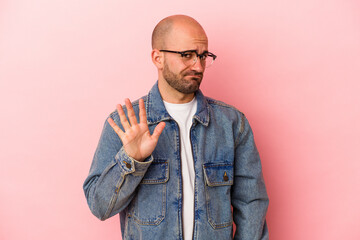 Young caucasian bald man isolated on pink background  rejecting someone showing a gesture of disgust.