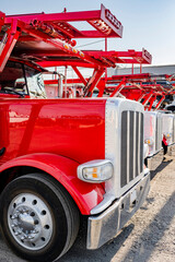 Bonnet red big rigs car hauler semi trucks with hydraulic semi trailers standing in row on the industrial parking lot