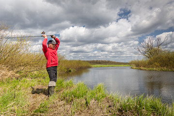 Fisher with a fishing rod stands on the river bank.