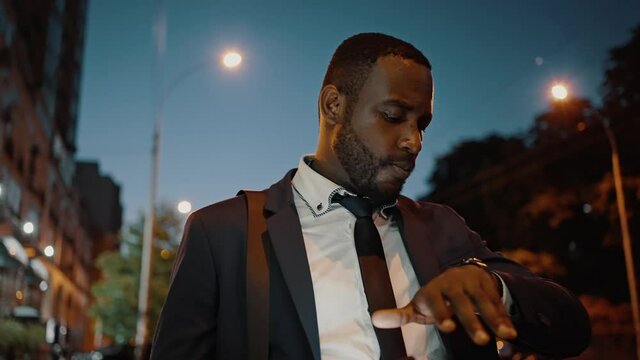 Late business meeting. Zoom out portrait of puzzled african american businessman calling taxi online on smartphone