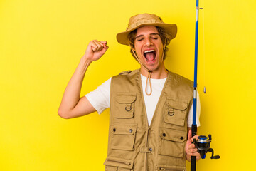 Young fisherman with makeup holding rod isolated on yellow background  raising fist after a victory, winner concept.