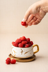Raspberries in a cup with human hand in the frame dropping fruit 