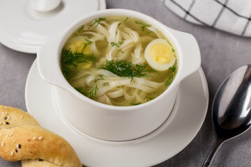 Chicken soup with noodles and egg in bowl with spoon on table
