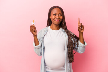 Young african american pregnant woman holding pacifier isolated on pink background showing number one with finger.