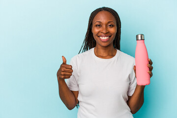 Young african american woman holding canteen isolated on blue background smiling and raising thumb up