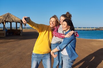 Fototapeta na wymiar Happy two middle aged women and girl child taking selfie on smartphone, sea beach background