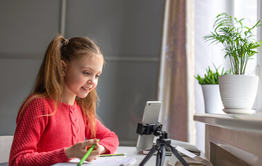 Little girl of european appearance looks at the smartphone screen at home with smile. Kids online, technology, online education, home studying and communication concept