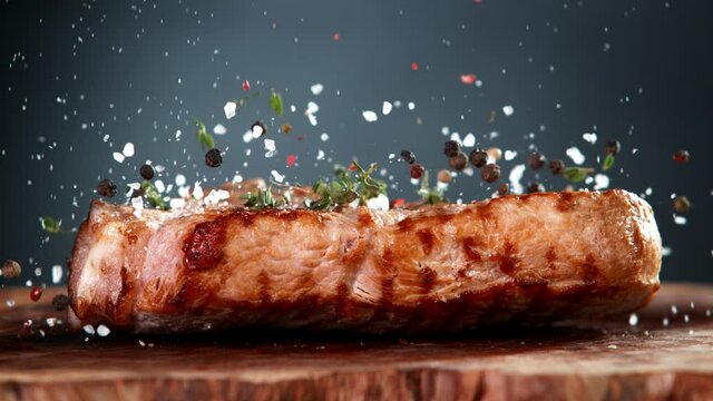 Super Slow Motion Shot of Falling Fresh Grilled Meat Steak and Seasoning on Wooden Board at 1000fps.