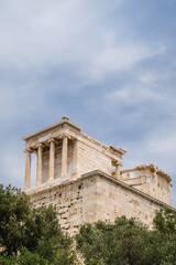 Fototapeta na wymiar Bottom view of the ancient Greek temple on the Acropolis in Athens, Greece. Antique architecture. Blue cloudy sky. Green trees.