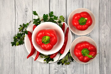 Red Bulgarian and red Chili peppers on white plates and a gray wooden table.