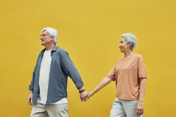 Pop color side view portrait of modern senior couple holding hands outdoors while walking against...