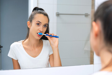 Yooung woman brushing her teeth at mirror