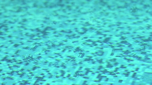 Closeup of swimming pool with rain drops making ripples on the on the surface of the water