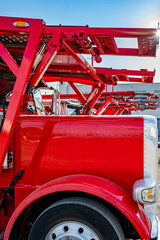 Side view of red big rig car hauler semi trucks with semi trailers standing in row on the parking lot at sunshine