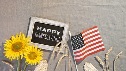 Happy Thanksgiving text on blackboard. Banner with USA flag, sunflowers, wheat ears, seasonal flowers. American Fall harvest festival. Flat lay, top view on beige textile .