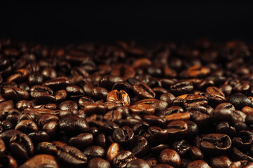 Fototapeta premium Coffee beans close up. The concept of making aromatic strong coffee on a black background in a low key. Discreet photography.
