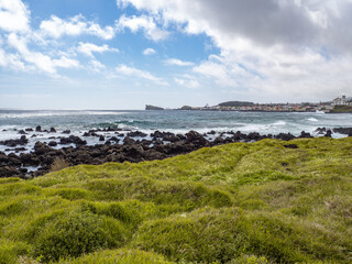 landscape of peaceful beach in shore with rocks and waves in blue ocean next to city in island of são miguel, açores, azores, portugal	
