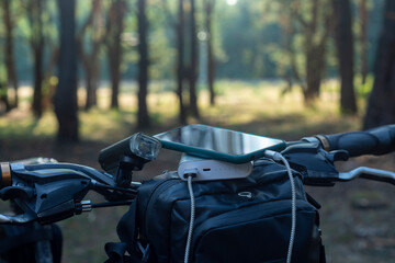 Smartphone is charged using a portable charger. Power bank in the forest on the background of a bicycle.