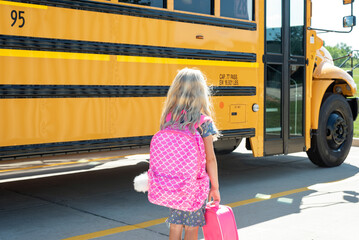 Little girl with pink backback standing by school bus