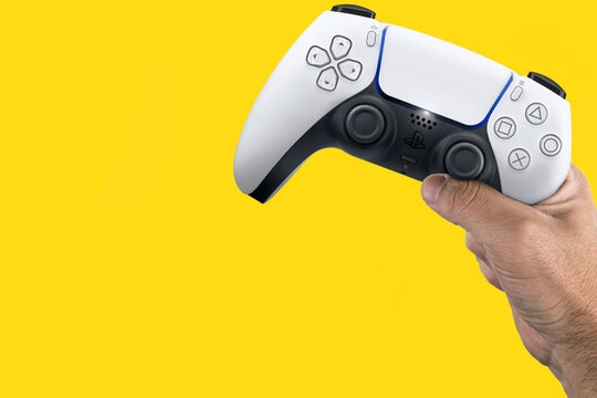 Male hand holding a Playstation 5 Dual Sense Controller isolated on yellow background. Rio de Janeiro, RJ, Brazil. June 2021.