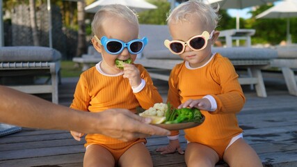 Hand serving plate of vegetables for twin toddles at the pool side. Healthy snacks for children 
