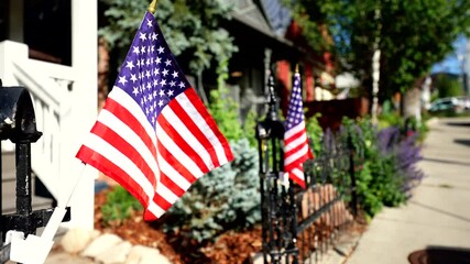 American flag Old Glory waves in a breeze in front of a house with a fence along a sidewalk on 4th of July