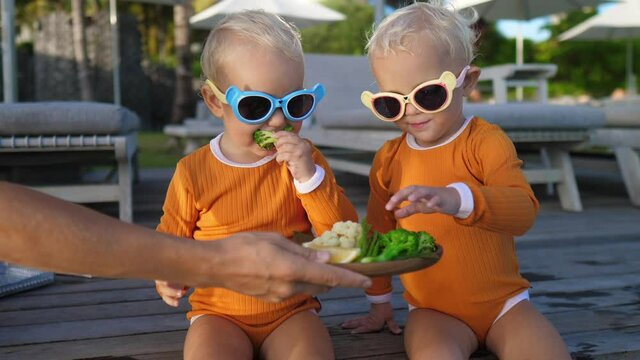 Hand serving plate of vegetables for twin toddles at the pool side. Healthy snacks for children 