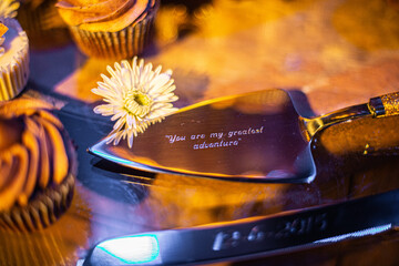 Silver cake serving utensils engraved with the phrase "You are my greatest adventure" at wedding reception cake table
