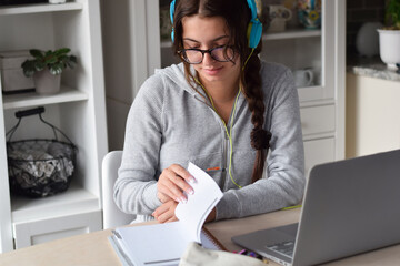 Young girl student in headphones studying at home using laptop computer