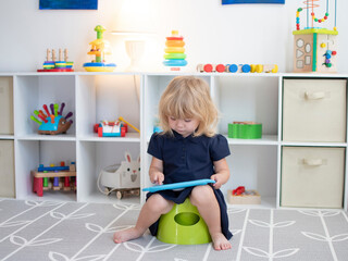 White toddler sitting on a potty with the tablet