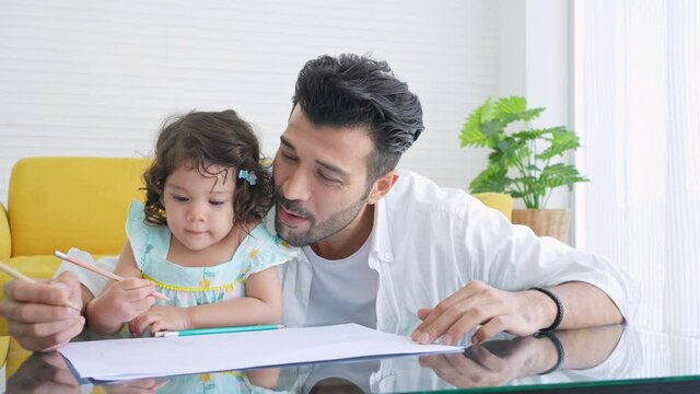 Happy family father teach little daughter using color pencil drawing on paper book in living room. Dad and cute child girl kid enjoy and having fun leisure activity and homeschooling together at home