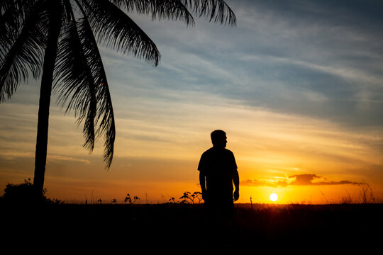 Beautiful sunset with silhouettes of a figure of a man with palm trees.