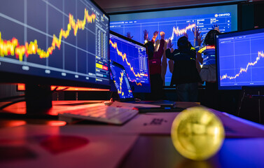 Happy broker trader hold hand up for victory when bitcoin value growth and receive profit on trading cryptocurrency in front big screen analysis graph chart in trade room full of computer and laptop